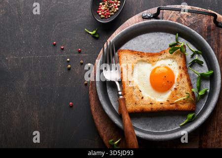 Valentines day breakfast. Fried eggs and bread in the shape of a heart and fresh vegetables on old wooden rustic background. Breakfast with surprise for loved ones. Mock up. Stock Photo
