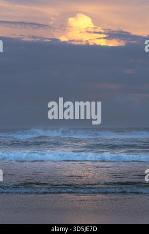 Sunset over the ocean beneath dramatic clouds, with golden light ...