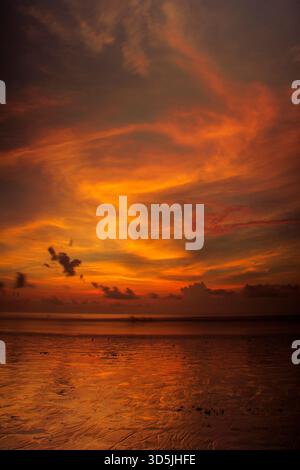 Partly cloudy dramatic orange sky over the Indian Ocean at sunset, Kuta Beach, Bali, Indonesia Stock Photo