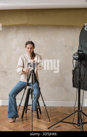 Female Photographer sitting on a stool in a photography studio setting up her camera on a tripod Stock Photo