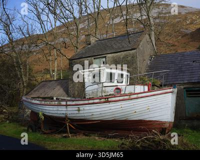 weathered Fishing Boat Resting Beside An Old Stone House with Mount Errigal as backdrop in Dunlewey County Donegal Ireland 02/11/2025 Stock Photo