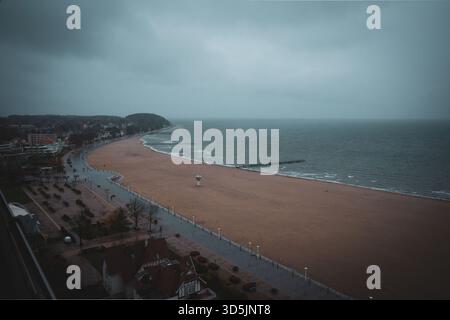 A moody coastal landscape showing a deserted beach on a cloudy, overcast day. The shoreline curves gently along the calm sea, with waves softly reachi Stock Photo
