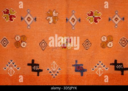 Close-up of a traditional Berber rug with colorful handwoven geometric motifs. Detailed texture of an orange Moroccan Berber carpet. Stock Photo