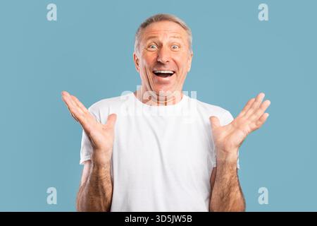 Happy Mature Man Expressing Excitement With Arms Raised Against a Blue Background Stock Photo