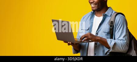 Young Man Smiling While Using Laptop Against Bright Yellow Background in Modern Setting Stock Photo