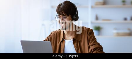 Young Man Smiles While Working on Laptop in Modern Home Office During Daytime Stock Photo