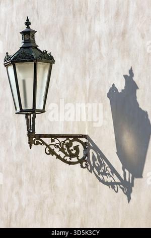 A historic iron street lamp hangs on the wall and casts a shadow Stock Photo