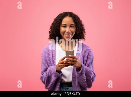 Cheery Young Black Lady Enjoying Smartphone on Pink Background While Working Remotely Stock Photo