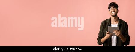 Young Man Smiles While Holding a Tablet Against a Pink Background in a Casual Setting Stock Photo