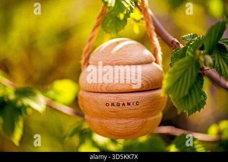 A wooden object with the word organic written on it is hanging from a hazelnut tree branch. The object is round and has a rope attached to it. The sce Stock Photo