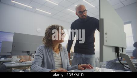 Diverse Mature Students Practice Digital Skills Under Male Teachers Supervision in Bright Computer Class. Concept Inclusion, Upskilling, Continuous Learning, and Digital Empowerment. High Angle. Stock Photo