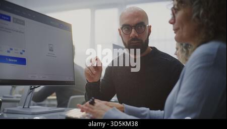 In Modern Computer Lab, Young Teacher Demonstrates Adult Student How Write Prompts For AI Generate Futuristic City Image. Concept of Innovation in Education, AI Literacy, Creative Technology Skills. Stock Photo