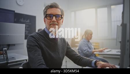 Stylish Senior Man With Glasses Works Attentively at Desktop Computer During Programming Course. Concept Continuous Learning, Modern Education, Technology Engagement, and Self Development. Portrait. Stock Photo