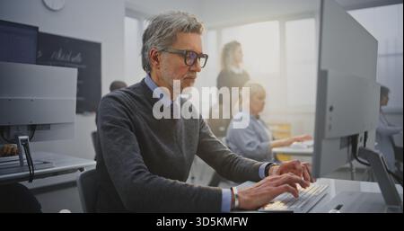 Stylish Senior Man With Glasses Works Attentively at Desktop Computer During Programming Course. Concept Continuous Learning, Modern Education, Technology Engagement, and Self Development. Portrait. Stock Photo