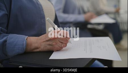 Close Up of Senior Woman Taking Written Test, Pen Moving Across Worksheet. Adult Student Writing Exam. Concept of Adult Learning, Skill Improvement, Academic Evaluation, and Focused Practice. Stock Photo