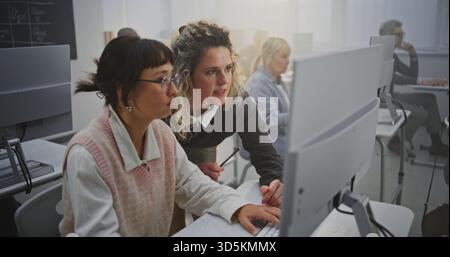 Confident Middle Aged Woman Instructor Supports Adult Female Learner in Computer Lab, Discussing Programming Assignments and Giving Feedback. Concept Lifelong Learning, Digital Literacy, Mentorship. Stock Photo