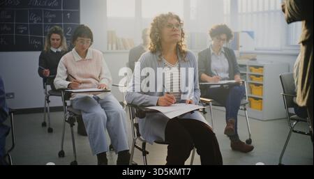 Group of Men and Women of Different Ages Participating in Classroom Activity. Focused Adult Students Write Notes During Teachers Lecture. Concept Professional Training and Lifelong Learning. Stock Photo