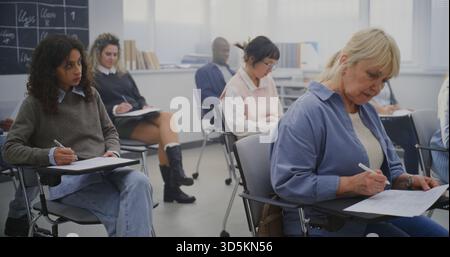 Mature Students Working on Assignments in Bright Contemporary Classroom Environment. Concept Adult Education, Lifelong Learning, Diversity, and Continuous Professional Development. Dolly Shot. Stock Photo