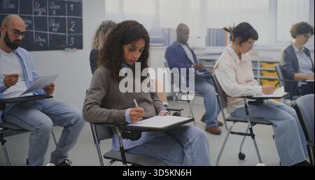 Mature Students Working on Assignments in Bright Contemporary Classroom Environment. Concept Adult Education, Lifelong Learning, Diversity, and Continuous Professional Development. Dolly Shot. Stock Photo