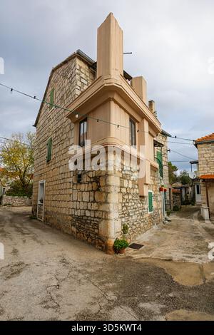 A charming stone-walled building on a quiet Mediterranean street, featuring green shutters, beige facade, and string lights. Rustic, timeless village Stock Photo