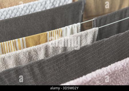 Close-up view of multiple colorful towels with different textures and patterns hanging neatly on indoor drying rack, emphasizing fabric softness and c Stock Photo