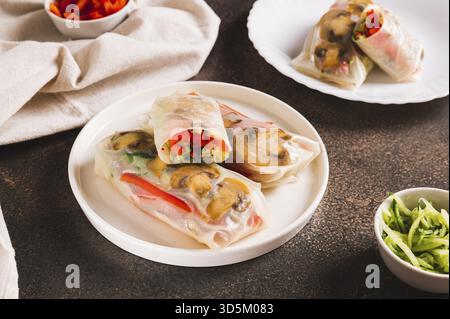 Delicious spring rolls with vegetables and mushrooms in rice paper on a plate on the table Stock Photo