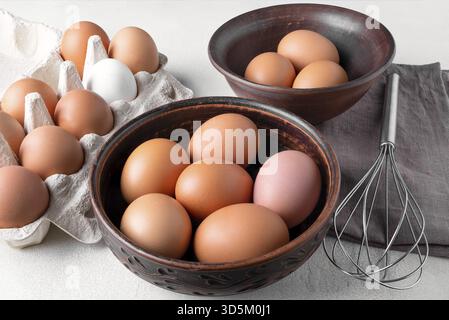 Brown chicken eggs in a cardboard packing container, and in a bowl on a table with a whisk to beat the eggs Stock Photo