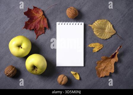 Top view mockup autumn composition of dry leaves, apples and walnuts. White notepad with blank sheets for text. Selective focus Stock Photo