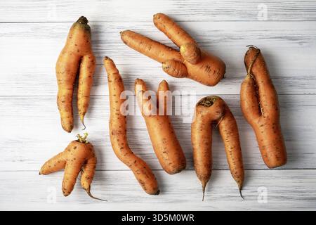 Several ripe orange ugly carrots lie on a light wooden surface. Selective focus Stock Photo