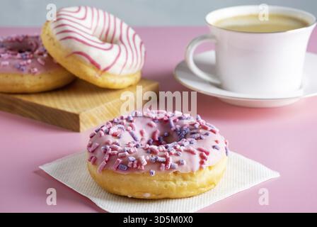 Three delicious fresh glazed donuts and cup of fresh hot coffee on pink background. Selective focus Stock Photo