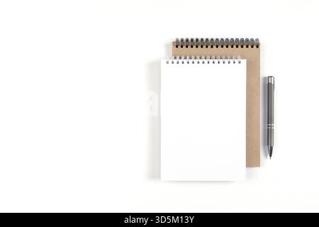 Two blank spiral notepads stacked on a white background next to an automatic pen. Notebooks with white and recycled sheets. Education, office Stock Photo