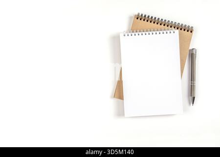 Two blank spiral notepads stacked on a white background next to an automatic pen. Notebooks with white and recycled sheets. Education, office Stock Photo