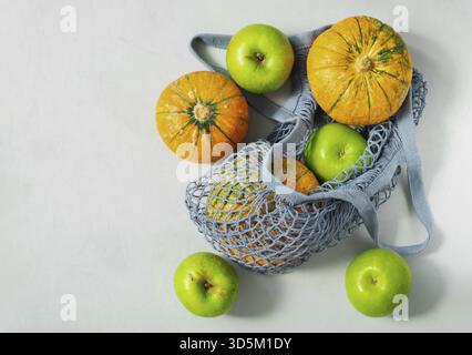 Small ripe pumpkins and green apples in an ecological string bag. The concept is plastic free, environmental protection, healthy lifestyle. Horizontal Stock Photo