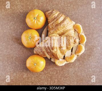 Delicious fresh croissants with vibrant oranges and sliced tangerines on wooden board Stock Photo