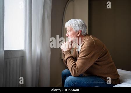 Thoughtful serious sad elderly man resting head on arms looking into distance with detached gaze Stock Photo