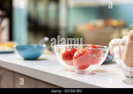 Empty kitchen with pizza ingredients laid out on a kitchen island. Bowl of tomatoes and sauce placed beside spices and utensils on the countertop, cozy space for homemade food preparation. Stock Photo