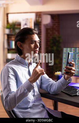 Focused businessman using hand gestures during project discussion with colleague during late night video call from home office. Male entrepreneur works remotely on strategy ideas across time zones. Stock Photo