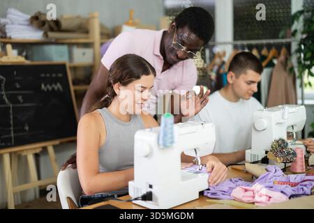 Middle-aged male teacher helping students sew Stock Photo