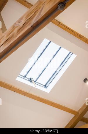 Skylight roof window set in a white sloped ceiling with exposed oak beams in a historic UK home, creating a bright loft space Stock Photo