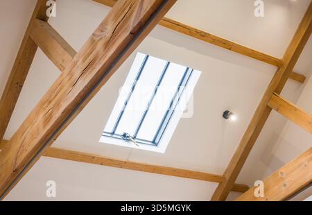 Skylight roof window set in a white sloped ceiling with exposed oak beams in a historic UK home, creating a bright loft space Stock Photo