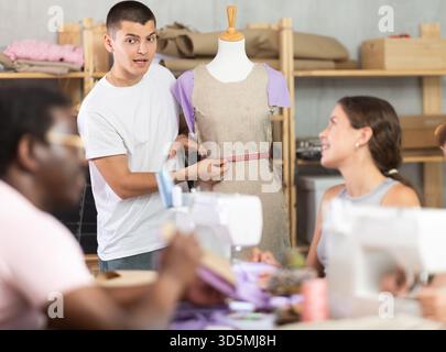 Young sewing instructor guiding adult beginners during practical workshop Stock Photo