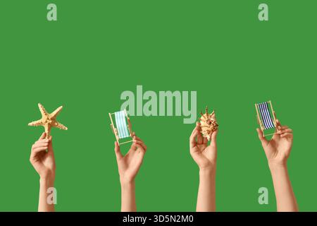 Female hands holding mini deck chairs with seashell and starfish on green background Stock Photo