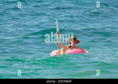 Woman floating turquoise ocean holding tablet on pink inflatable ring during summer vacation holidays Stock Photo