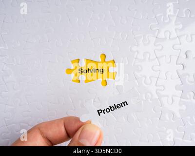 Hand placing a white puzzle piece labeled “Problem” into a yellow missing spot revealing the word “Solving.” Concept of problem-solving, strategy, log Stock Photo