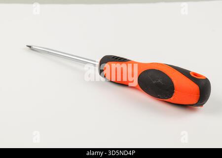 A close-up view shows a screwdriver resting on a plain white surface. The tool features an orange and black rubber handle, designed for a comfortable Stock Photo