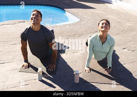 Couple practicing yoga by pool, enjoying morning sun and stretching together Stock Photo