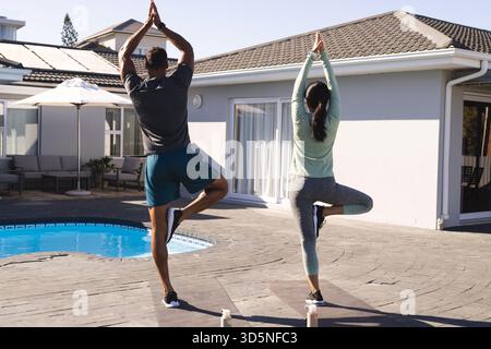 Couple practicing yoga by poolside, enjoying morning exercise and relaxation Stock Photo