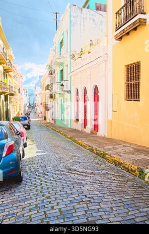 A narrow cobblestone street is flanked by colorful buildings, including pastel blues, yellows, and whites. Stock Photo