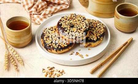 three donuts with chocolate and peanut toppings on a white square ceramic plate Stock Photo