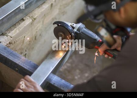 Focused worker using an angle grinder for cutting metal, creating bright spark in an industrial workshop. This construction craft requires skill and s Stock Photo